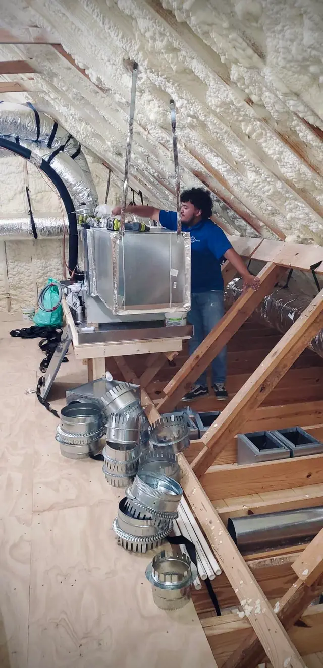 Technician fitting a new air handler in an attic with fresh duct collars laid out