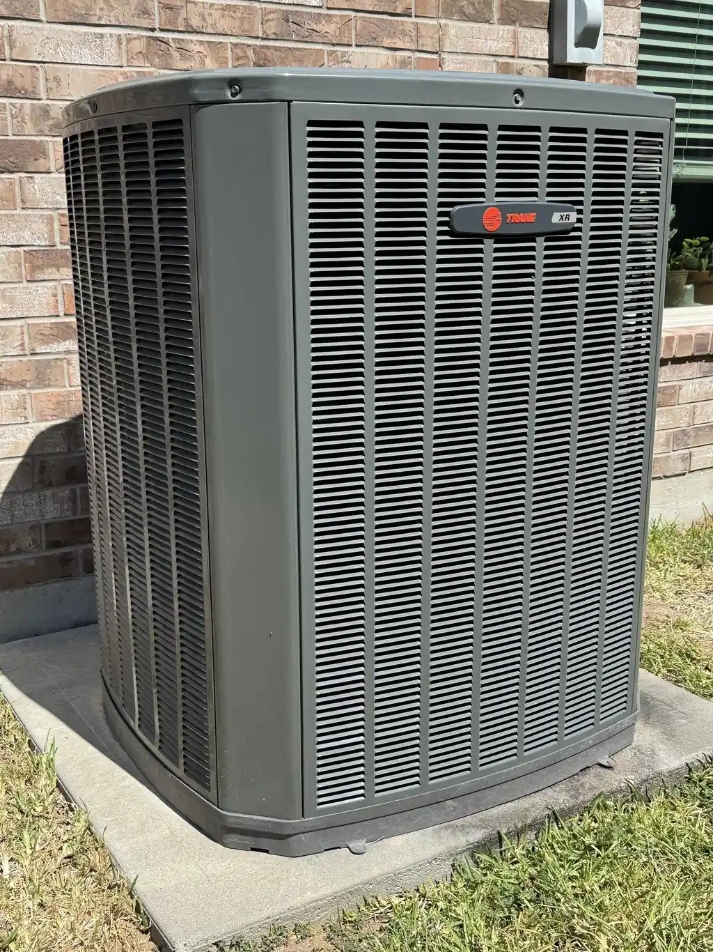 New Trane XR condenser on a fresh pad against a brick wall